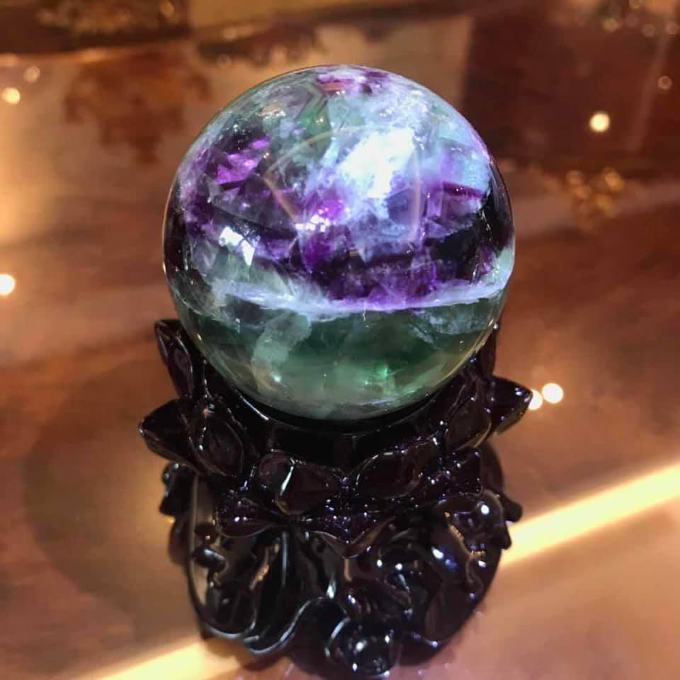 深色木座上的螢石球，紫綠色帶狀紋理